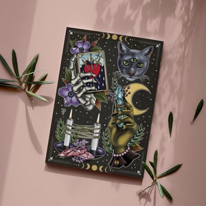 May include: A dark, illustrated print featuring occult imagery. The artwork includes a three-eyed cat, a skeleton hand holding a card with a heart, a hand holding a crystal, candles, and crescent moons. Purple flowers and green leaves accent the design.