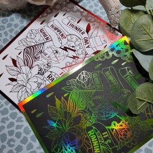 Peut inclure: Deux impressions holographiques sur fond noir avec un motif vert et rouge. Le motif représente une bouteille avec un éclair et le texte "THUNDER ONLY HAPPENS WHEN IT'S RAINING".