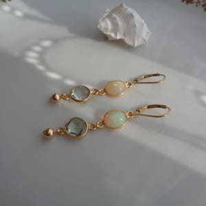 Könnte beinhalten: Ein Paar goldene Ohrringe mit einem tropfenförmigen Opal und einem kleineren, runden, hellblauen Edelstein.