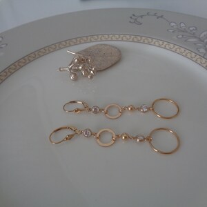 Könnte beinhalten: Ein Paar goldene Ohrringe mit kleinen klaren Steinen und runden Akzenten.