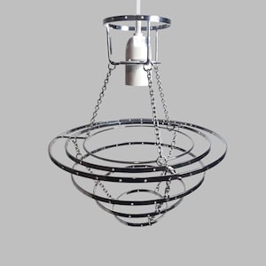 Puede incluir: Una lámpara de araña moderna con acabado cromado, con una serie de anillos circulares concéntricos suspendidos por cadenas. La lámpara tiene una carcasa central para la bombilla y un diseño minimalista, adecuada para la iluminación interior.