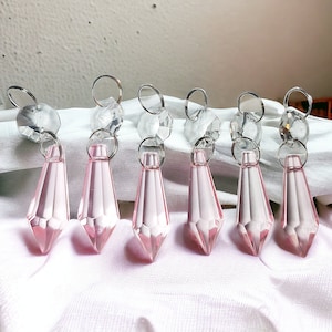 Puede incluir: Siete prismas de araña de cristal rosa en forma de lágrima con conectores de metal plateado.