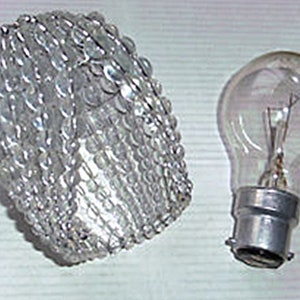 May include: A clear glass light bulb cover with a decorative beaded design. The cover is designed to fit over a standard light bulb.