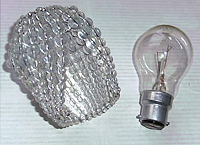 May include: A clear glass light bulb cover with a decorative beaded design. The cover is designed to fit over a standard light bulb.