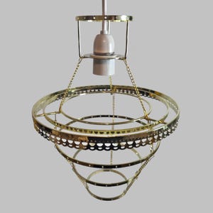 May include: A vintage gold-coloured pendant light fitting. The light has a series of concentric circular rings forming a cone shape. The top has a bulb holder and is suspended by a chain. The fitting is designed with a decorative, openwork pattern.