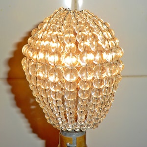 May include: A clear glass lampshade made of small round beads, with a light bulb inside, illuminating the beads.