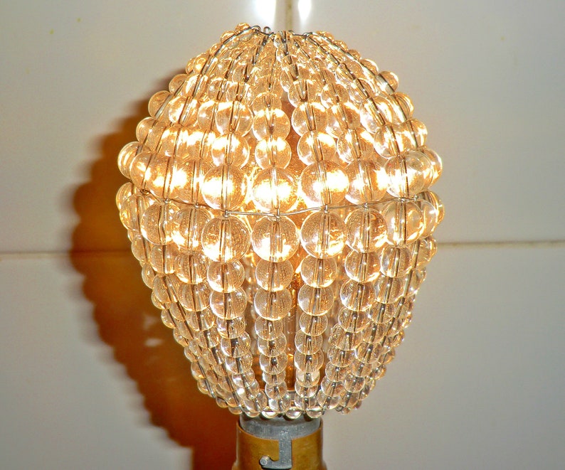 May include: A clear glass lampshade made of small round beads, with a light bulb inside, illuminating the beads.