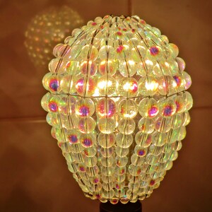 May include: A round iridescent lampshade made of glass beads. The beads are strung together on a wire frame and create a shimmering effect.