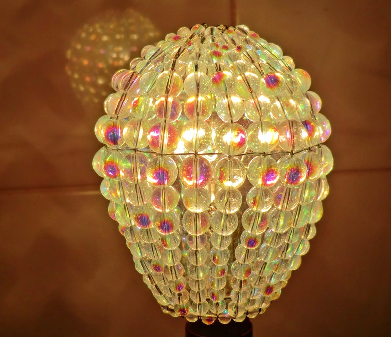 May include: A round iridescent lampshade made of glass beads. The beads are strung together on a wire frame and create a shimmering effect.