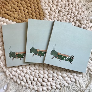 May include: Three light blue note cards with a green grasshopper illustration on each. The grasshoppers are drawn in a cartoon style with green and brown markings.
