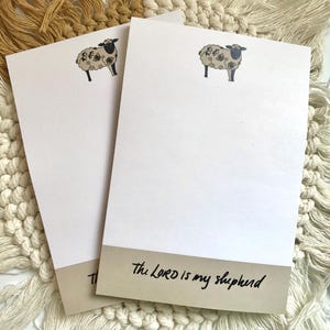 May include: Two white notepads with a black and white sheep illustration and the text "The Lord is my shepherd" on the bottom of one notepad.