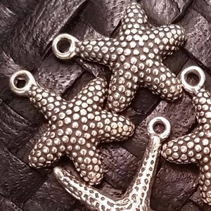 May include: Four silver starfish charms with a textured surface. The charms have a loop at the top for attaching to jewelry or other crafts.