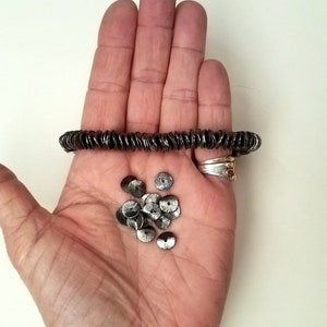 May include: A hand holding a strand of silver-colored metal beads and a pile of loose silver-colored metal beads.