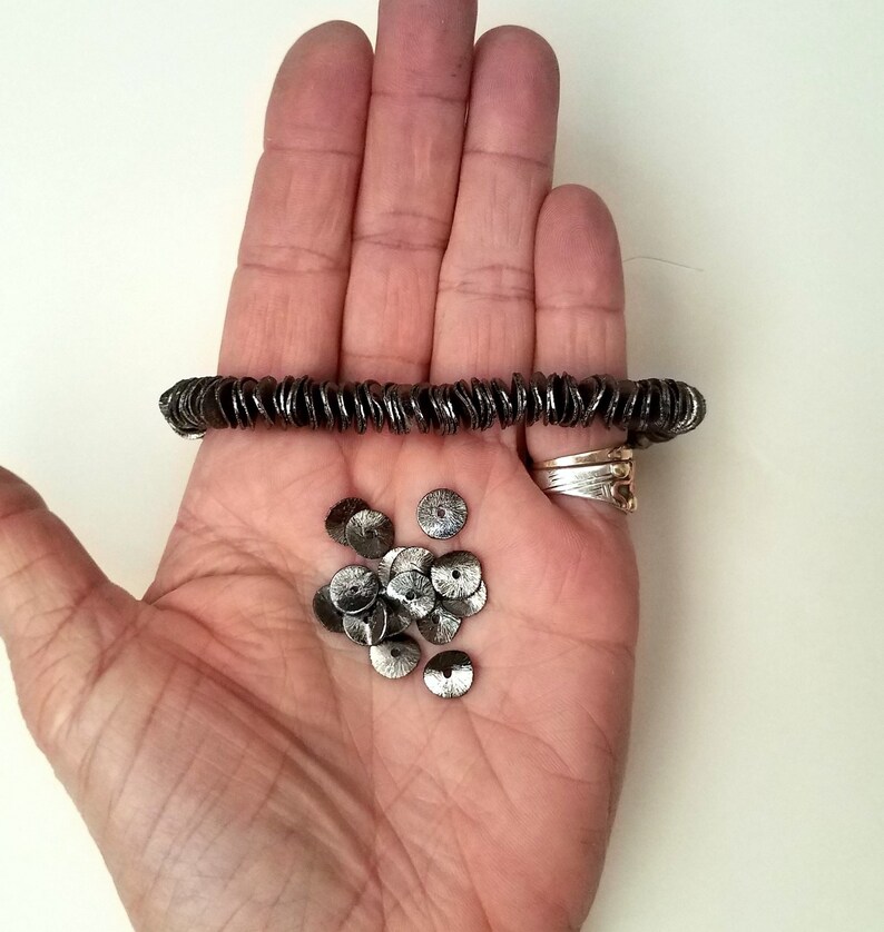 May include: A hand holding a strand of silver-colored metal beads and a pile of loose silver-colored metal beads.