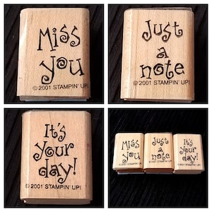 May include: Four wooden rubber stamps with different messages. The stamps are all rectangular and have a light brown color. The messages on the stamps are "Miss you", "Just a note", "It's your day!" and "Miss you, Just a note, It's your day!" The stamps are all copyright 2001 Stampin' Up!.