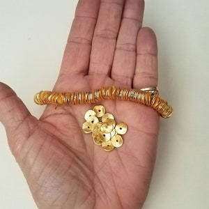 May include: A hand holding a strand of gold-colored metal beads and a pile of loose gold-colored metal beads.