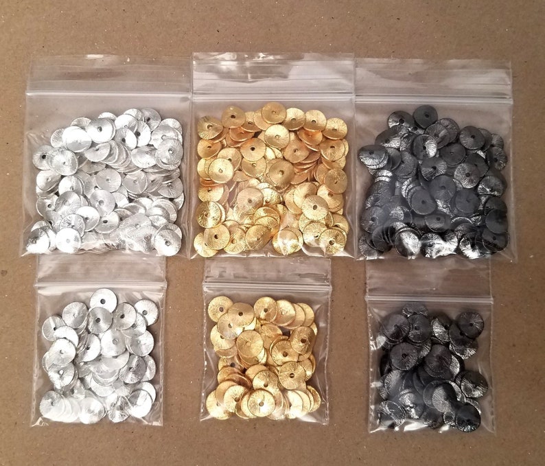 May include: Six small bags of metallic round sequins. The bags are clear plastic and contain silver, gold, and black sequins.