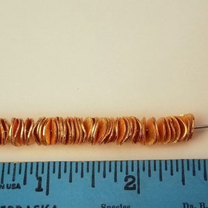 May include: A strand of gold-colored beads, approximately 2 inches long, strung on a silver wire. The beads are flat and have a slightly wavy texture.