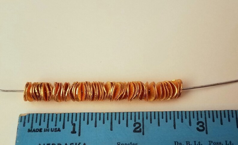 May include: A strand of gold-colored beads, approximately 2 inches long, strung on a silver wire. The beads are flat and have a slightly wavy texture.