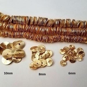 May include: Gold metallic round sequins in three sizes: 10mm, 8mm, and 6mm. The sequins are arranged in piles on a white surface.