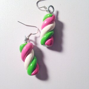 May include: A pair of earrings shaped like twisted candy canes. The candy canes are pink, white, and green.