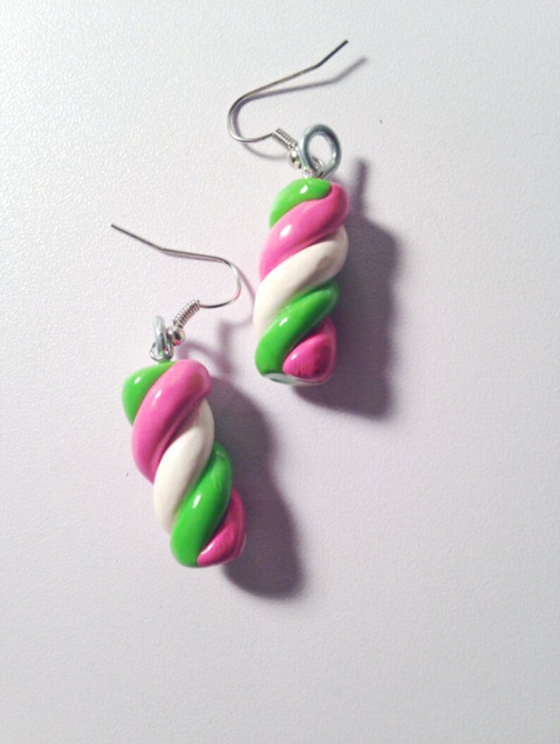 May include: A pair of earrings shaped like twisted candy canes. The candy canes are pink, white, and green.