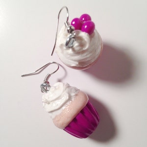 May include: A pair of cupcake earrings with pink and white frosting and pink sprinkles. One earring has a pink cupcake with white frosting and the other earring has a white cupcake with pink frosting.