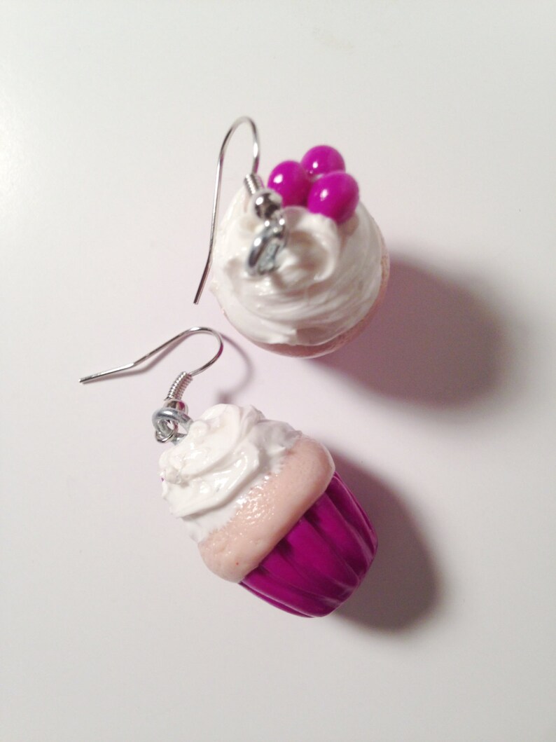 May include: A pair of cupcake earrings with pink and white frosting and pink sprinkles. One earring has a pink cupcake with white frosting and the other earring has a white cupcake with pink frosting.