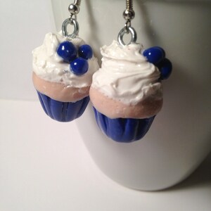 May include: A pair of blue and white cupcake earrings with white frosting and blue blueberry accents.