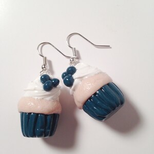 May include: A pair of dangle earrings featuring miniature cupcake charms. The cupcakes are teal blue with white frosting and blue sprinkles.