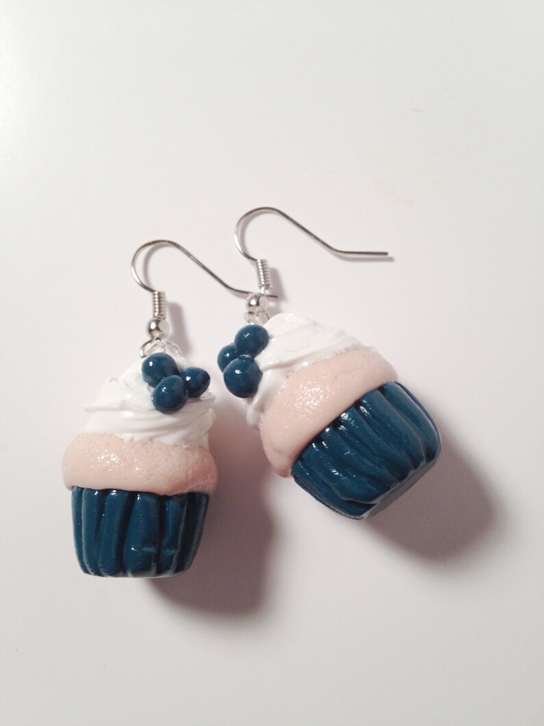May include: A pair of dangle earrings featuring miniature cupcake charms. The cupcakes are teal blue with white frosting and blue sprinkles.