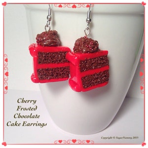 May include: A pair of red and brown cherry frosted chocolate cake earrings. The earrings are made of polymer clay and are shaped like a slice of cake with chocolate frosting and red sprinkles.