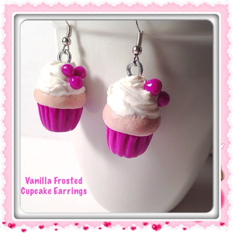 May include: A pair of vanilla frosted cupcake earrings with pink and white frosting and pink sprinkles. The earrings are made of polymer clay and have silver hooks.