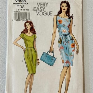 May include: A Very Easy Vogue sewing pattern, V8180, featuring illustrations of two dresses. One is a light green, short-sleeved dress, and the other is a blue dress with a floral pattern. The pattern size is DD (12-14-16-18).