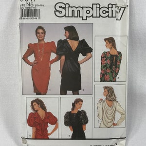 Pode incluir: Padrão de costura Simplicity com vários designs de vestidos. A capa mostra vestidos com detalhes como mangas bufantes, babados e costas drapeadas. O tamanho do padrão é N5 (10-18), equivalente a EUR N5 (38-46).