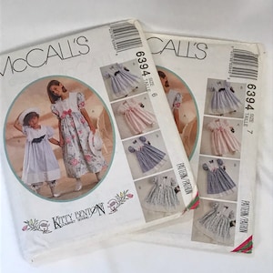 May include: Two McCall's sewing patterns for girls' dresses. The pattern on the left is size 6 and the pattern on the right is size 7. Both patterns feature floral prints and are designed by Kitty Benton.