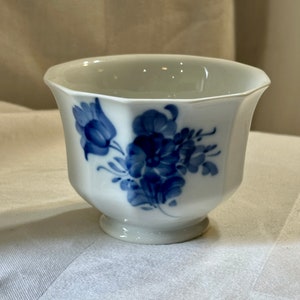 Könnte beinhalten: Eine weiße Porzellanschüssel mit blauem Blumendesign. Die Schüssel hat einen gewellten Rand und einen Fuß.