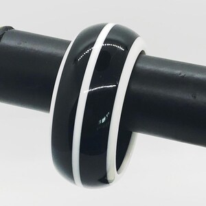 May include: Black and white bangle bracelet with two white stripes around the circumference.