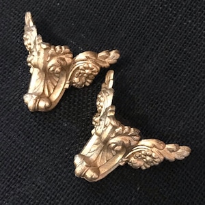 May include: Two gold-toned metal corner brackets with ornate floral designs. The brackets are shaped like a right angle and have a decorative, scroll-like design.
