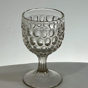 May include: Clear glass goblet with a textured, bubble-like pattern on the bowl. The stem is slender and the base is round. The glass is transparent, allowing light to pass through. This vintage-style glassware is suitable for serving wine or other beverages.