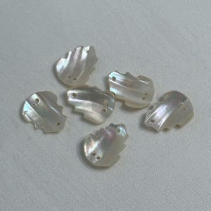 May include: Six iridescent white shell buttons with two holes each. The buttons are shaped like a leaf and have a wavy texture.