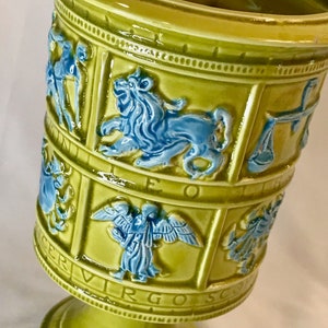 Peut inclure: Un vase en céramique vert avec un motif zodiacal. Le vase présente les signes astrologiques du Lion, de la Vierge, de la Balance et du Scorpion. Le vase est décoré d'un glaçage bleu et vert.