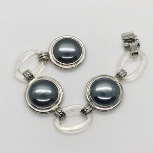 May include: A silver bracelet with three black round stones and clear plastic links.