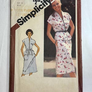 May include: A Simplicity sewing pattern envelope 9947 for a size 12 miss outfit. The cover features a white top and skirt set with a red and blue floral print, a black belt, and a matching illustration of the garment design on the left side.