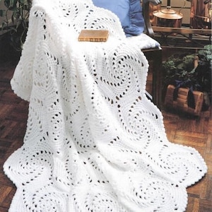 Pode incluir: Cobertor branco de crochê com um padrão circular. O cobertor está drapeado sobre uma cadeira com uma almofada azul.