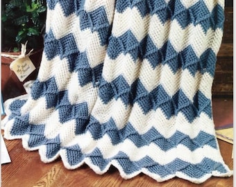 May include: A crocheted chevron blanket in white and blue. The blanket is folded and draped over a wooden surface.