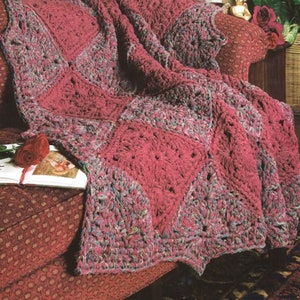 May include: A crocheted throw blanket in a deep pink color with a multi-colored pattern. The blanket is draped over a red couch with a floral pattern.