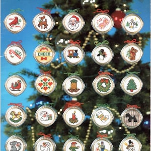 Op de afbeelding: Een verzameling van 50 kruissteek-ornamentpatronen met verschillende kerstthema's, waaronder kerstman, rendier, kerk, sneeuwpop, speelgoedtrein, sok, kaars, schommelpaard, krans, boom, peperkoekman, pinguïn, bel, snoepstok, hart, vogel en meer.  Ornaments To Treasure.