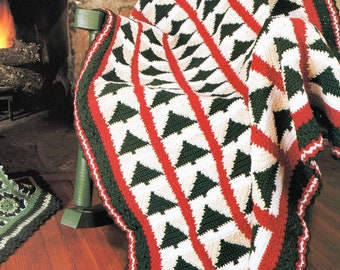 Può includere: Una coperta all'uncinetto con un motivo di alberi di Natale in verde, bianco e rosso. La coperta è drappeggiata su una sedia davanti a un camino.