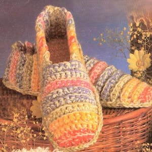 Może przedstawiać: Para  ręcznie robionych kapci z wielokolorowym paskowanym wzorem w odcieniach żółtego, pomarańczowego, różowego, fioletowego i zielonego.